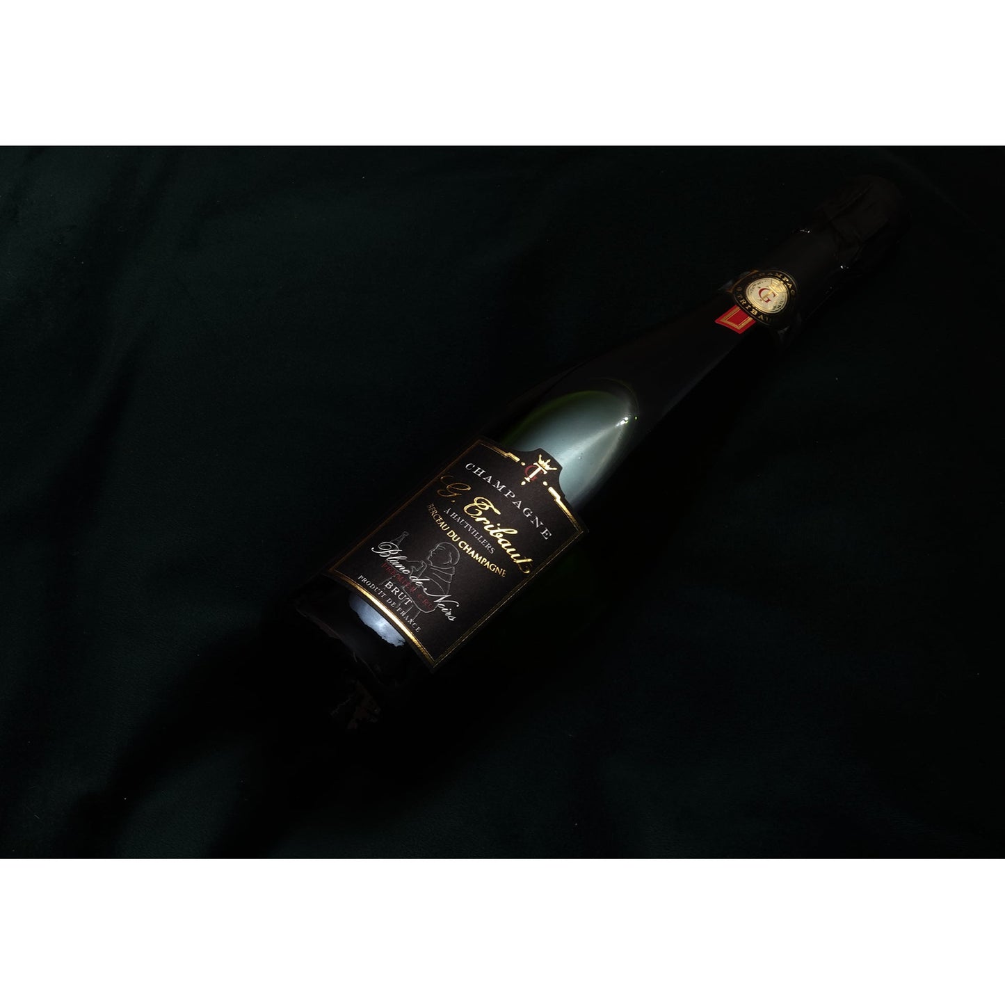 Groene fles champagne met zwarte hals en zwart label. In gouden letters staat: Champagne - G. Tribaut - a Hautvillers - Berceau du Champagne - Blanc de Noirs - Brut - Produit de France